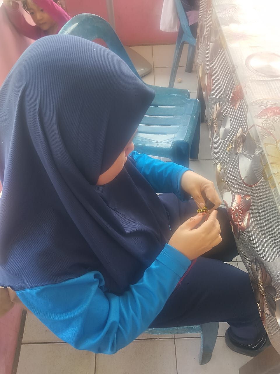 Peniaga craft sedang menyulam corak batik secara manual dengan benang merah di atas jalur anyaman hitam