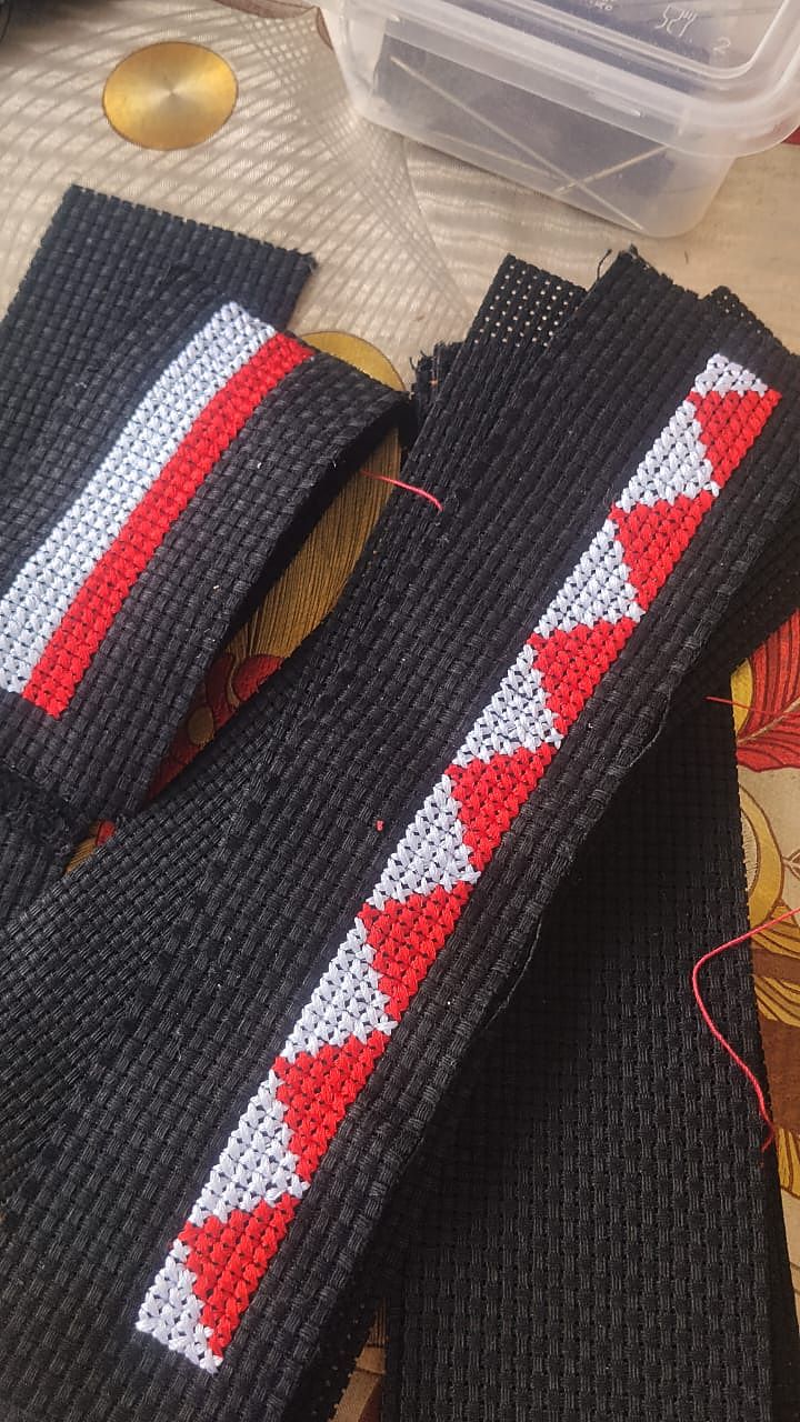 Dua jalur anyaman hitam siap dengan motif segi tiga merah dan putih disulam tangan